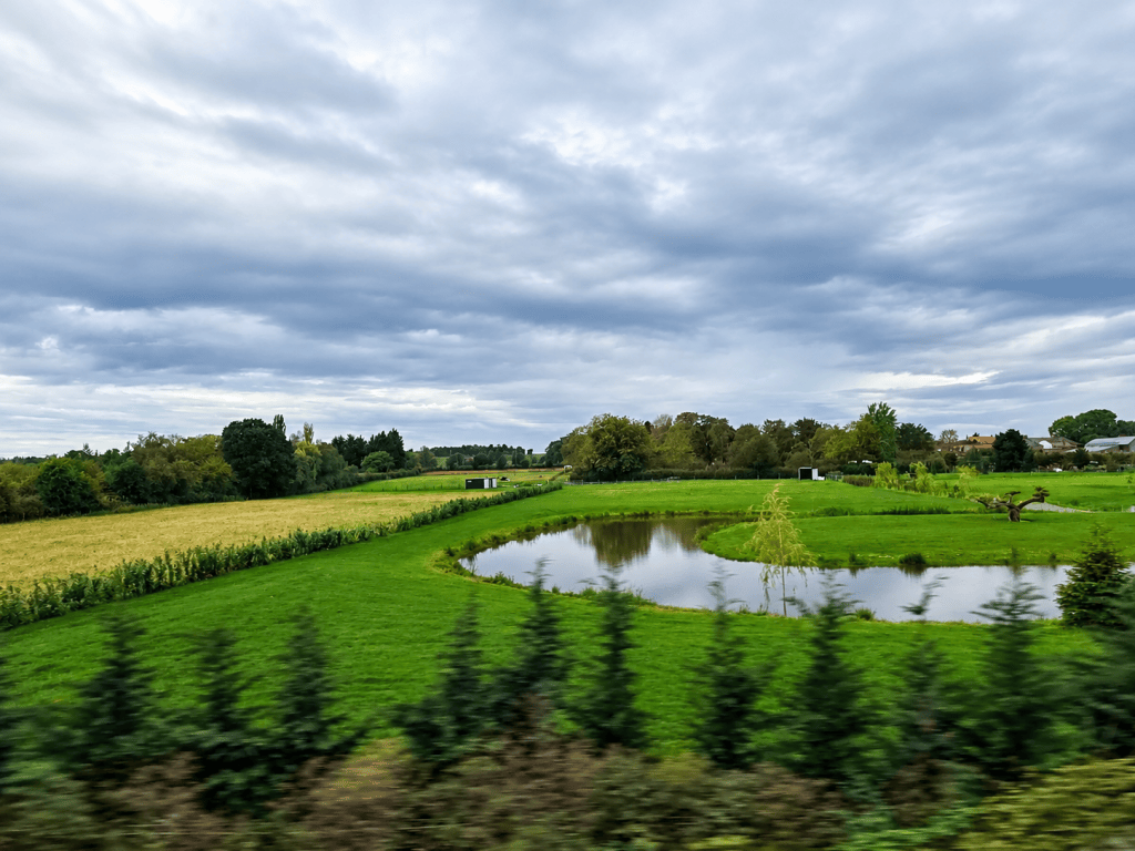 Green pastures surrounding quiet water in the English countryside, photographed from a moving train