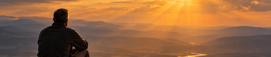 A man overlooking a vast mountain landscape as sunlight breaks through the clouds